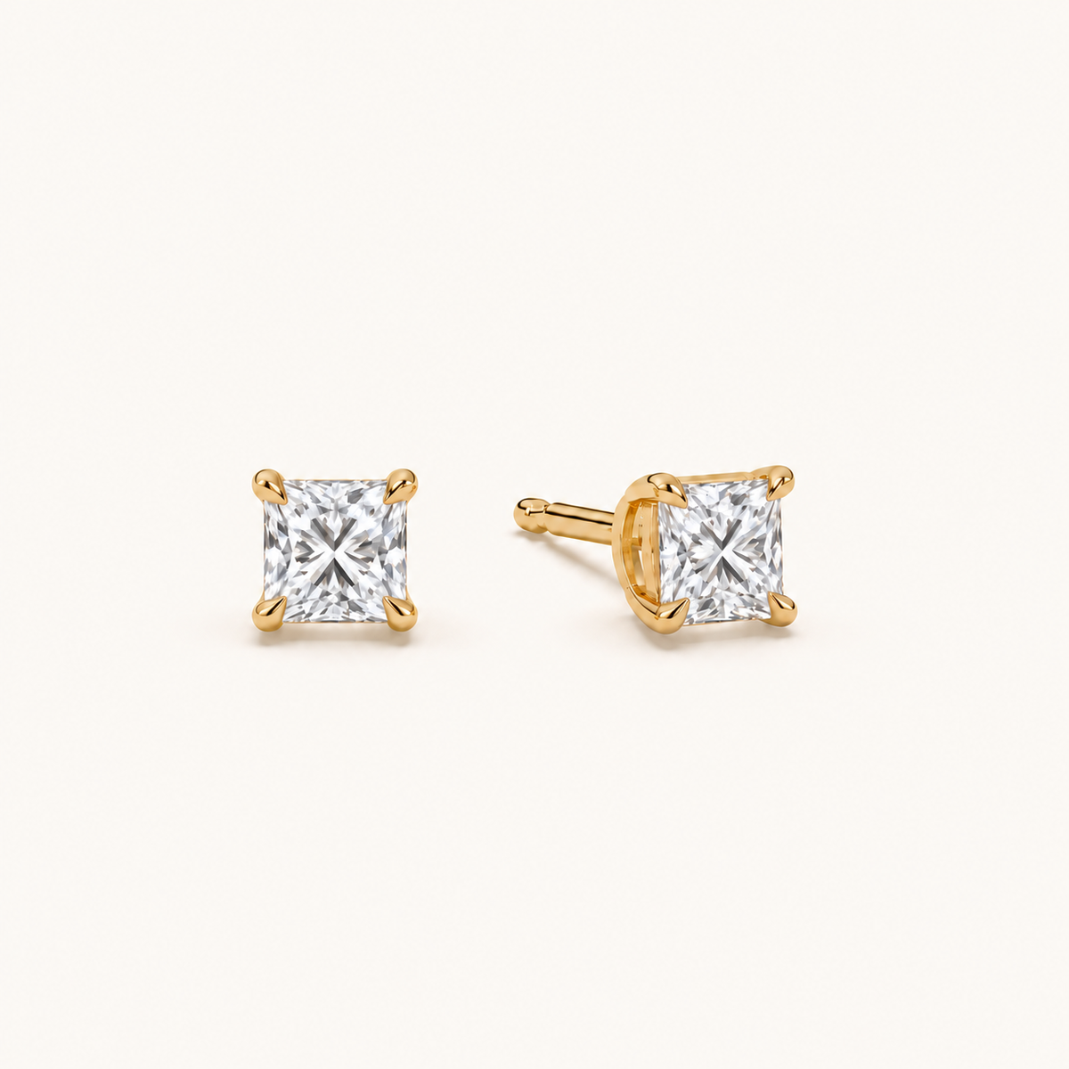 Princess diamond earrings, 1ct total pair weight, yellow gold, angled view on warm ivory