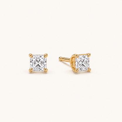 Princess diamond earrings, 1ct total pair weight, yellow gold, angled view on warm ivory
