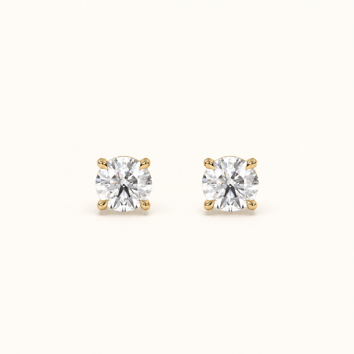 Round brilliant diamond studs in yellow gold, front pair view on warm ivory