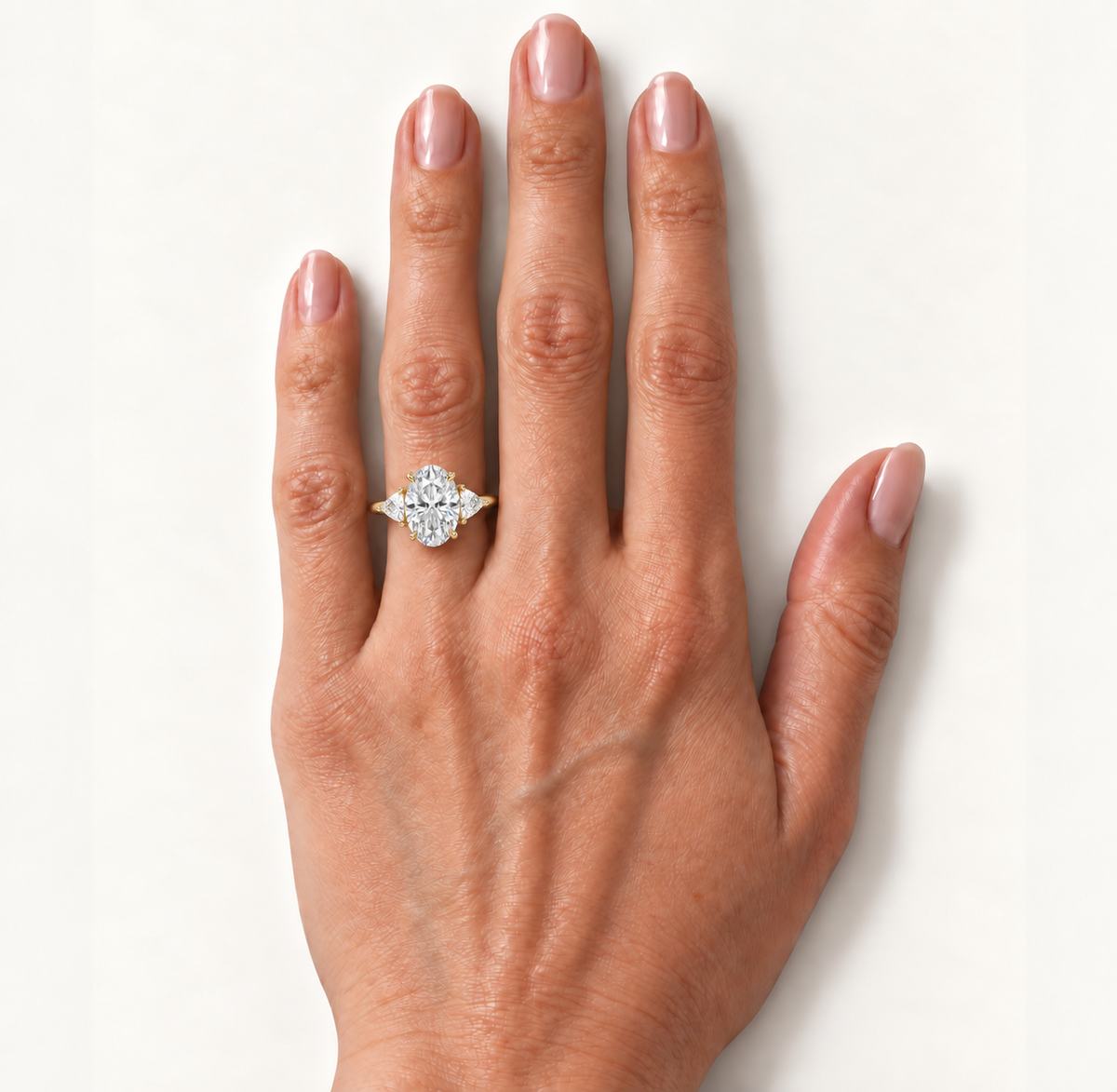 Oval diamond three-stone ring worn on the ring finger in yellow gold